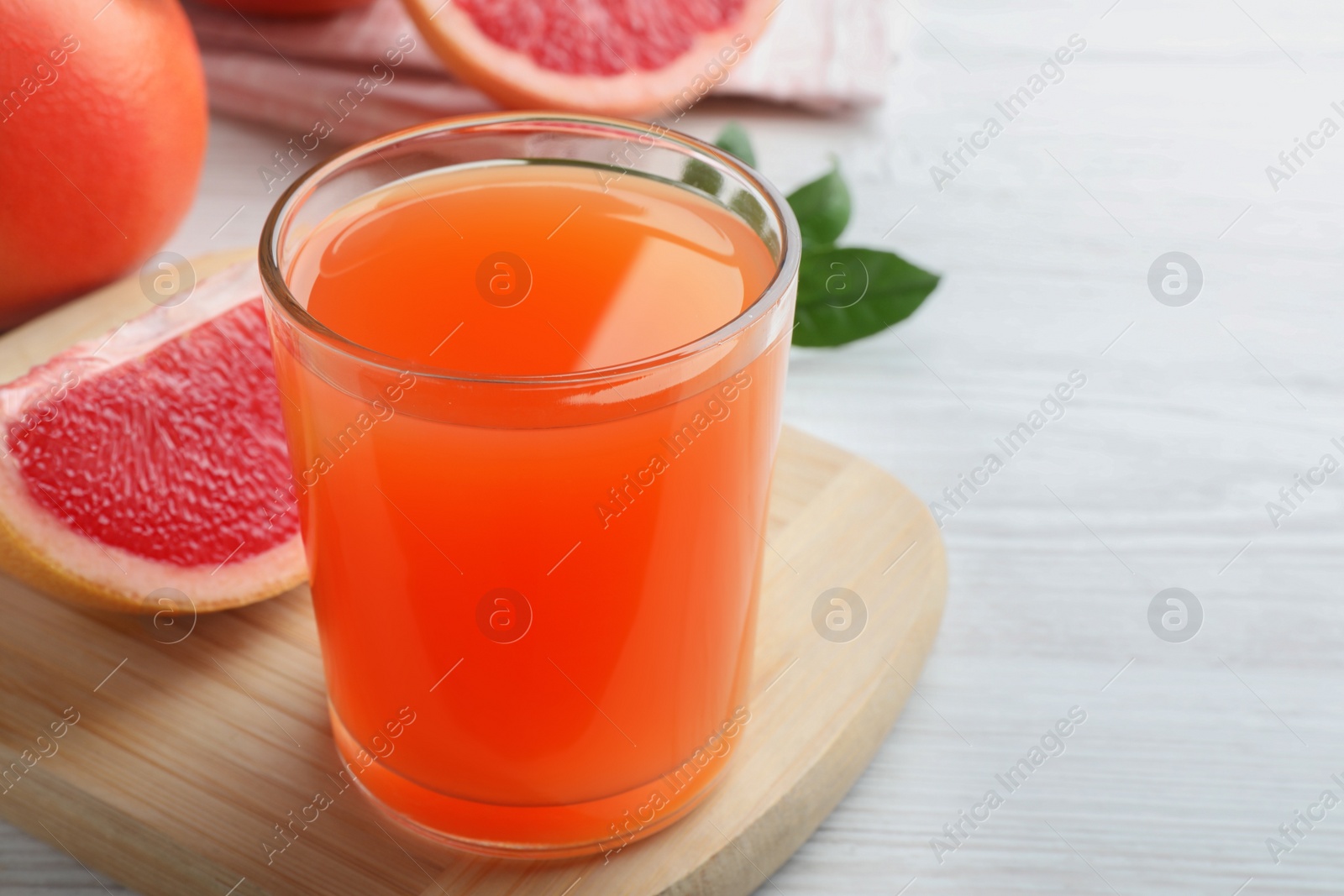 Photo of Tasty freshly made grapefruit juice on white wooden table. Space for text