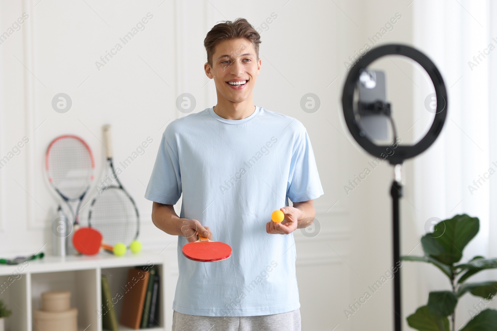 Photo of Smiling sports blogger with table tennis racket and ball streaming online fitness lesson at home