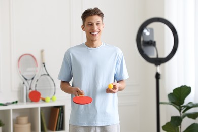 Photo of Smiling sports blogger with table tennis racket and ball streaming online fitness lesson at home