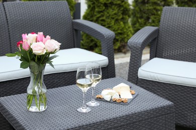 Vase with roses, glasses of wine and food on rattan table on outdoor terrace