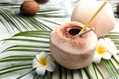Photo of Fresh coconut with drinking straws and flowers on white marble table, closeup