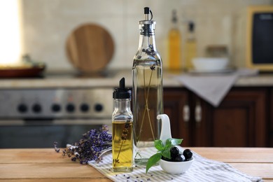 Photo of Different cooking oils, olives, basil and lavender flowers on wooden table in kitchen
