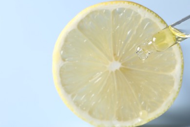 Dripping cosmetic serum from pipette onto lemon slice against light blue background, closeup. Space for text