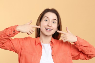 Portrait of smiling woman pointing at her dental braces on beige background