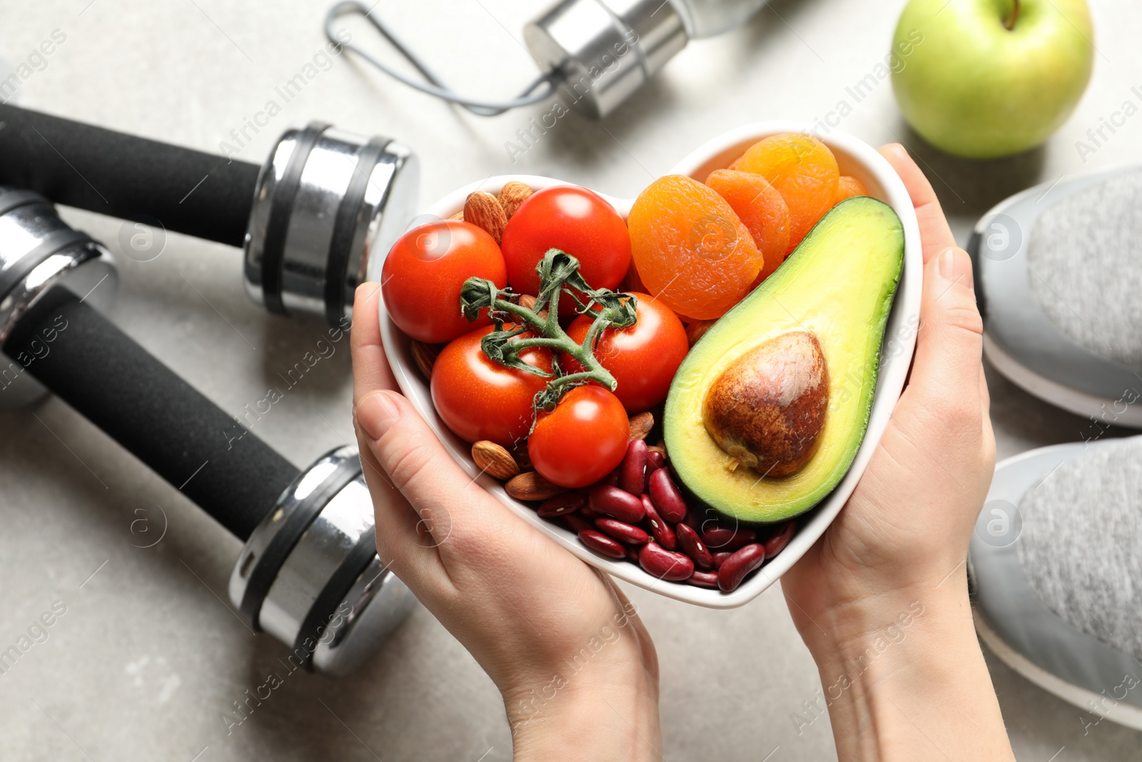 Photo of Woman holding heart-healthy products over table with sports equipment, top view