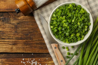 Photo of Chopped green onion in bowl on wooden table, flat lay. Space for text
