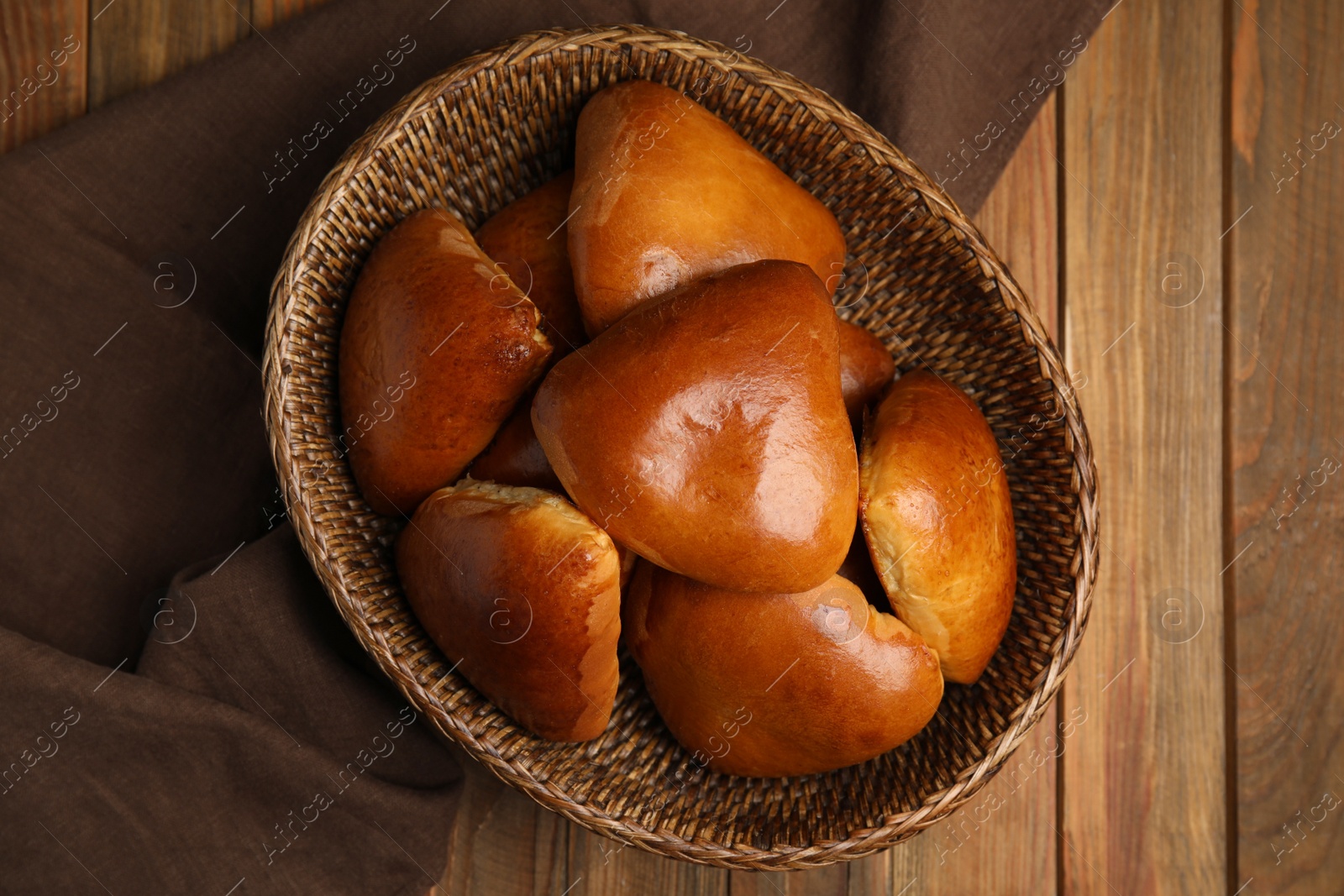 Photo of Wicker basket with delicious baked pirozhki on wooden table, flat lay