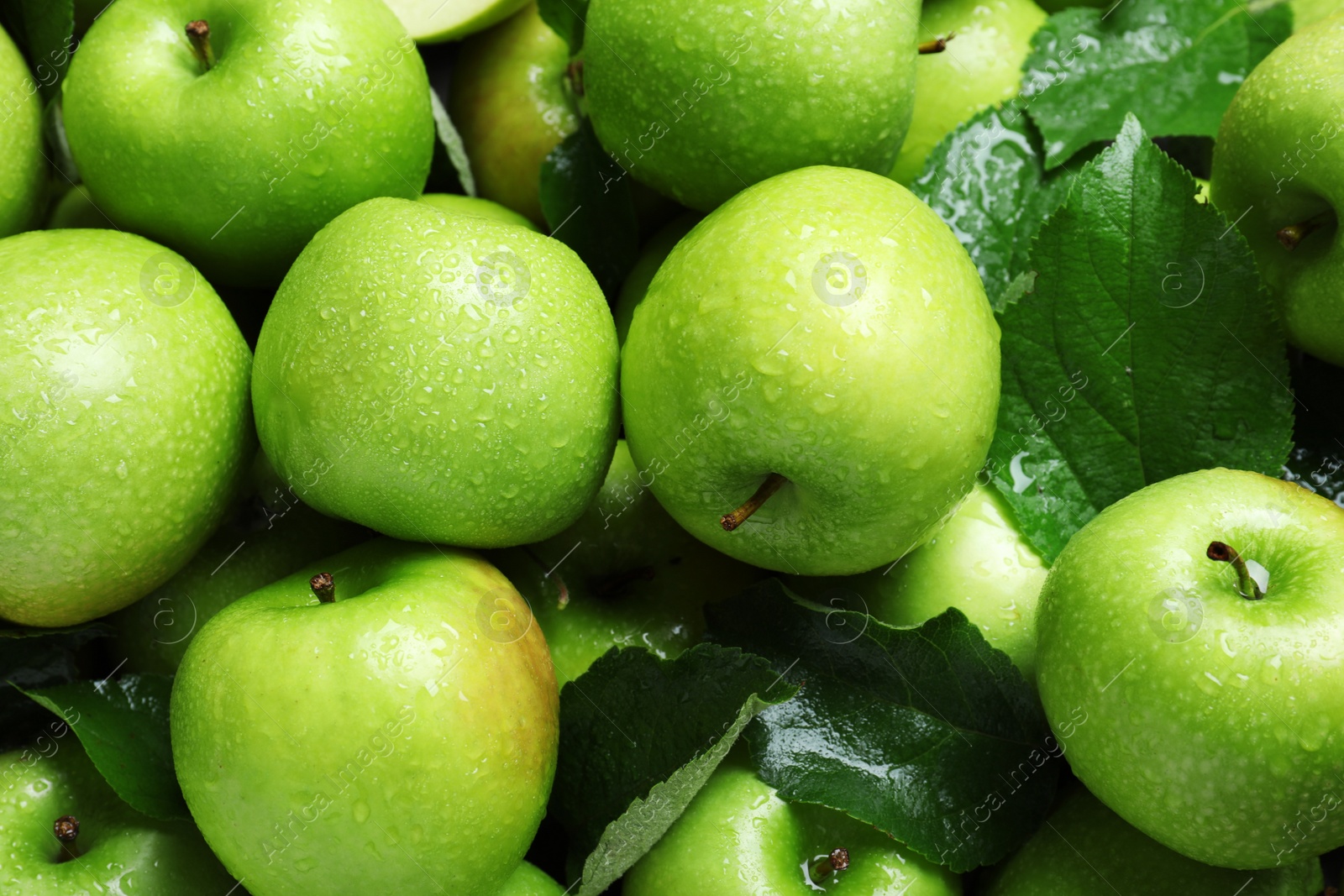 Photo of Pile of wet green apples with leaves as background, closeup