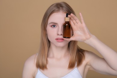 Beautiful young woman with bottle of essential oil on brown background