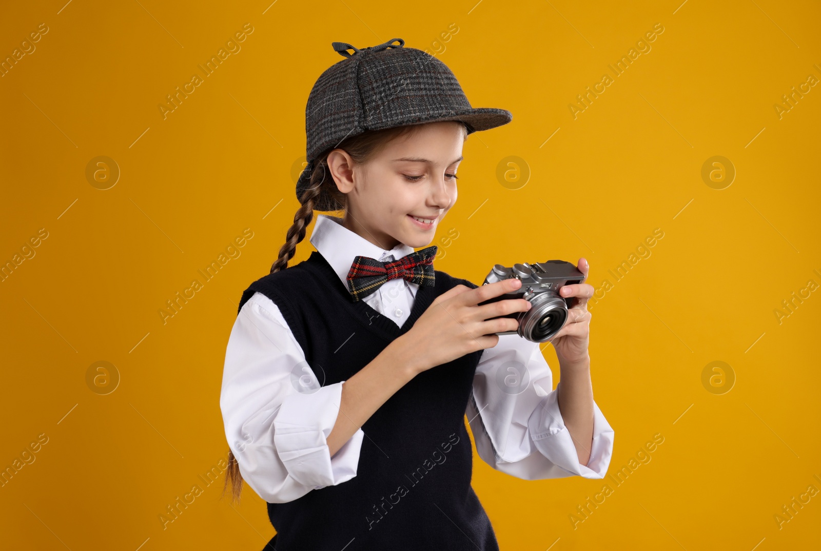 Photo of Cute little detective with vintage camera on yellow background