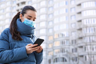 Photo of Woman with disposable mask and smartphone outdoors. Dangerous virus