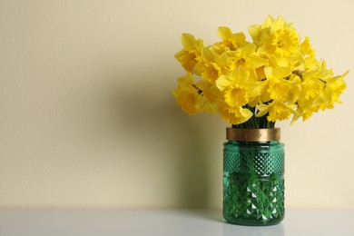 Photo of Beautiful daffodils in vase on white table near light wall, space for text