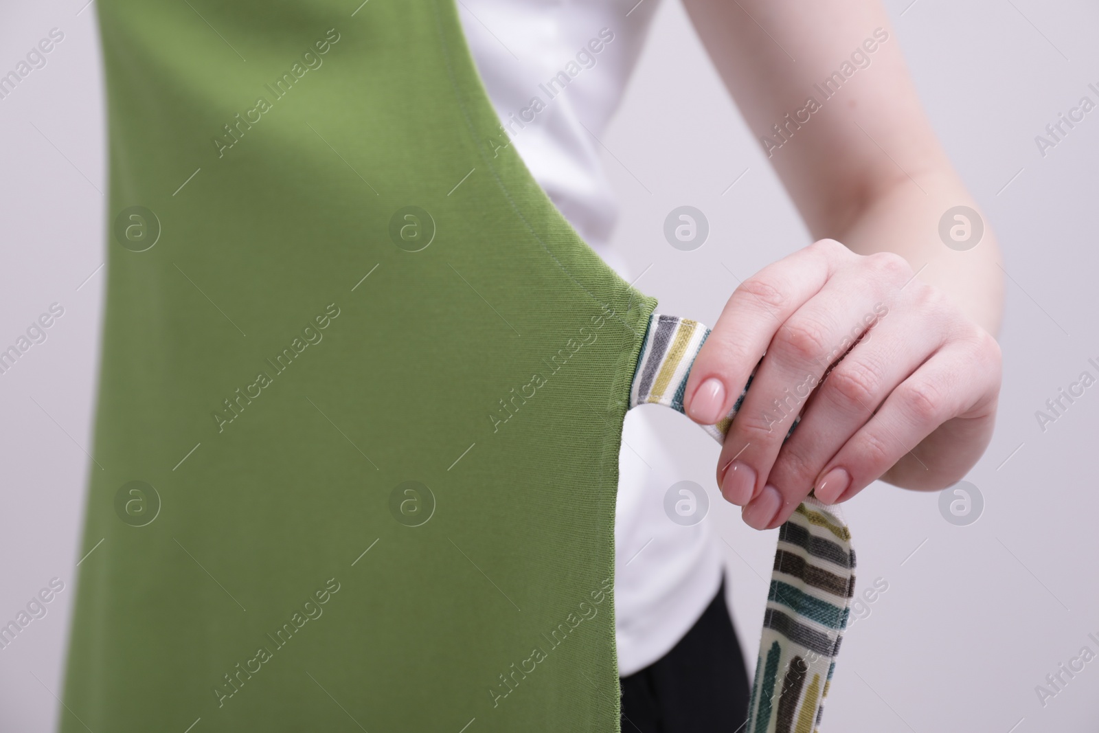 Photo of Woman putting on green apron against white background, closeup