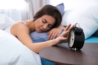 Photo of Young woman turning off alarm clock in morning. Bedtime