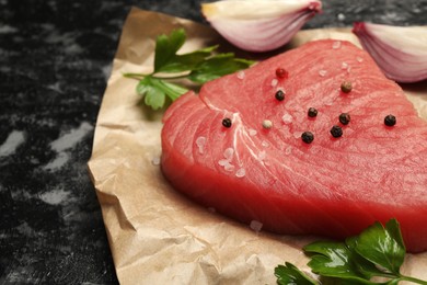 Photo of Raw tuna fillet with parsley and spices on black table, closeup