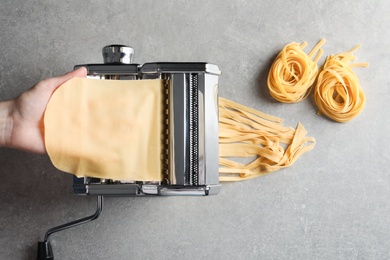 Young man preparing noodles on pasta maker at table, top view