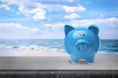 Image of Saving money for summer vacation. Piggy bank on stone surface near sea, space for text