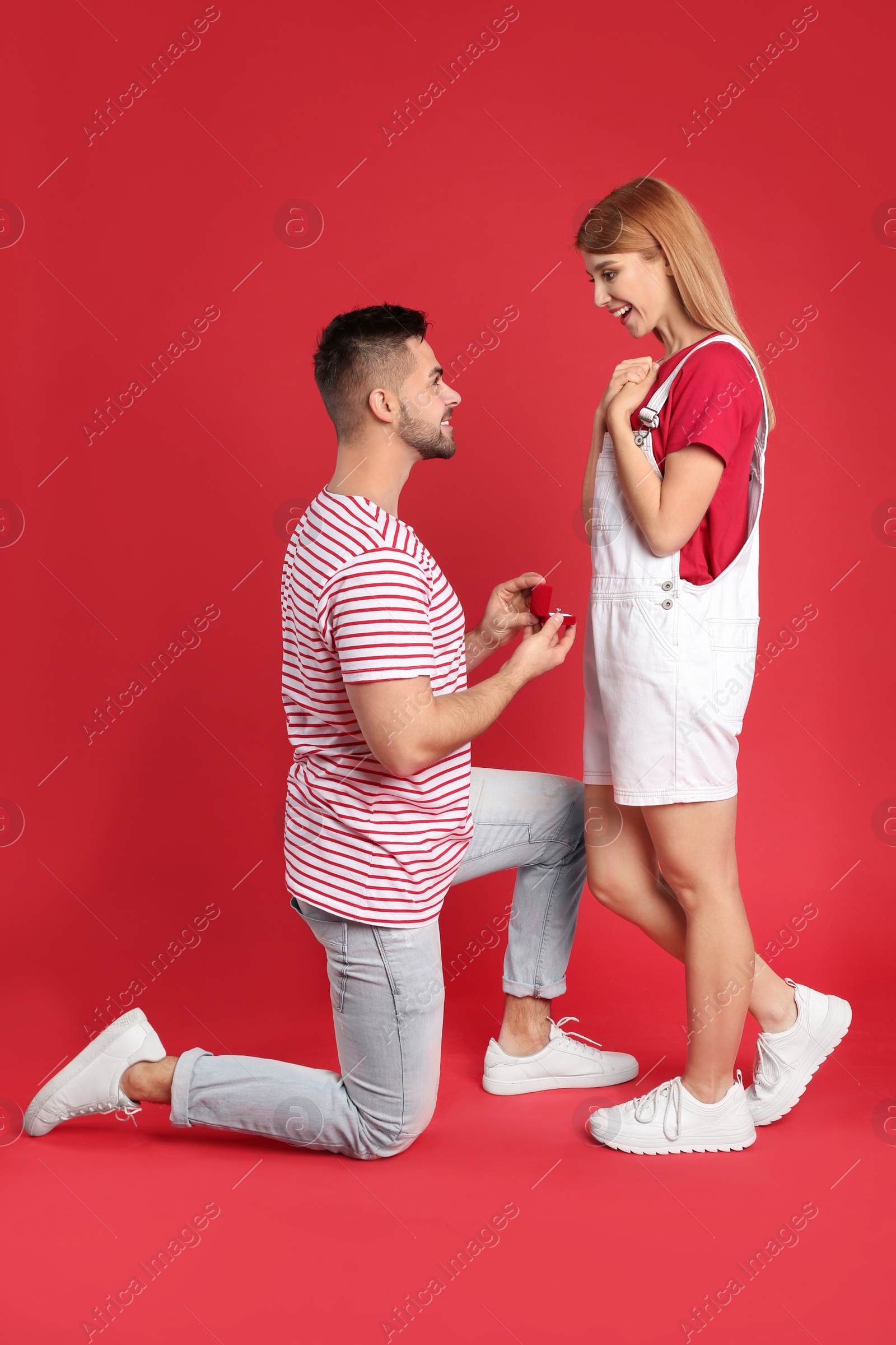 Photo of Man with engagement ring making marriage proposal to girlfriend on red background