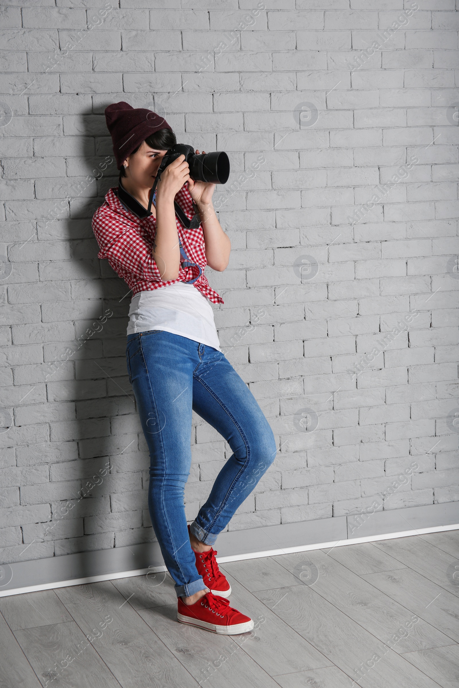 Photo of Young female photographer with camera near brick wall