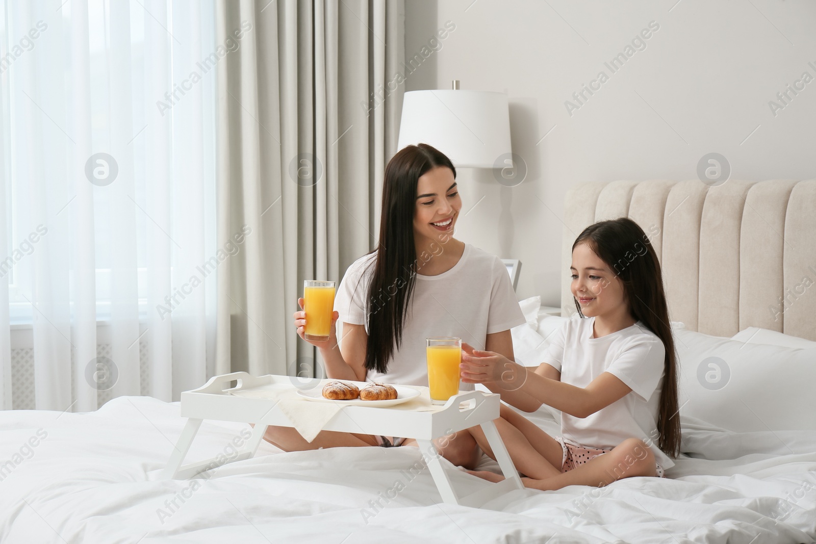 Photo of Young mother and her daughter having breakfast on bed at home