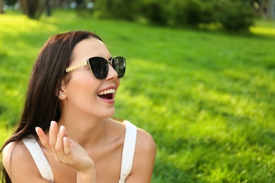 Beautiful young woman wearing stylish sunglasses in park. Space for text