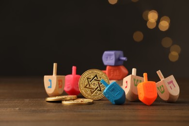 Photo of Dreidels with Jewish letters and coins on wooden table against blurred festive lights, selective focus. Space for text. Traditional Hanukkah game