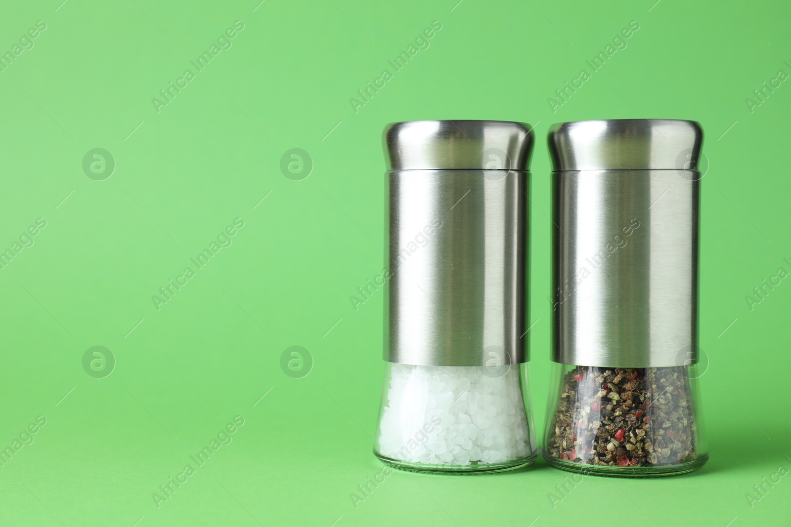 Photo of Salt and pepper shakers on green background, closeup. Space for text