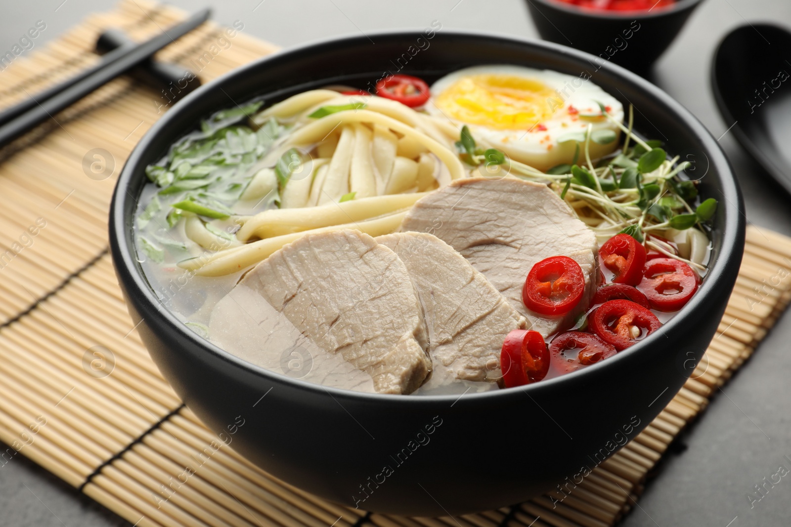 Photo of Delicious ramen with meat in bowl served on bamboo mat, closeup. Space for text. Noodle soup