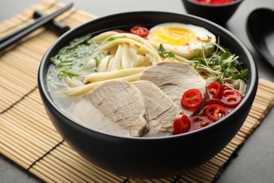 Photo of Delicious ramen with meat in bowl served on bamboo mat, closeup. Space for text. Noodle soup