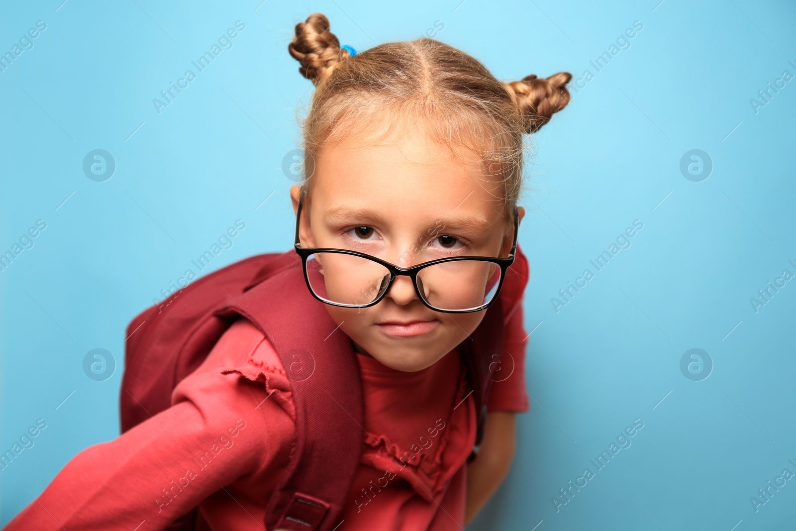 Photo of Funny little girl in glasses with backpack on light blue background