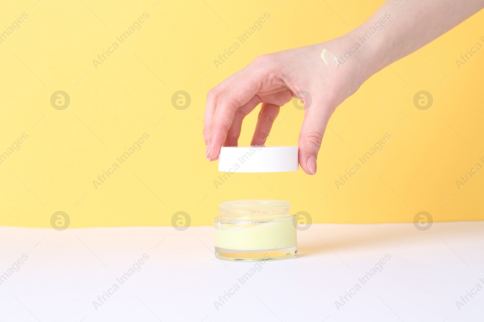 Photo of Woman with jar of cream on yellow background, closeup