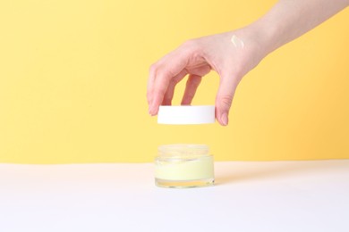 Photo of Woman with jar of cream on yellow background, closeup