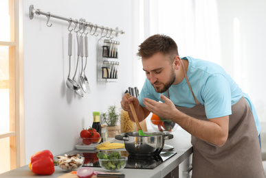 Young man cooking delicious soup in kitchen