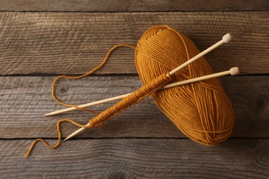 Soft orange yarn, knitting and needles on wooden table, top view