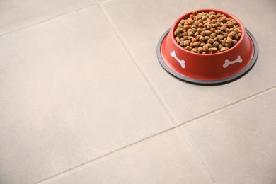 Photo of Dry dog food in feeding bowl on tiled floor. Space for text