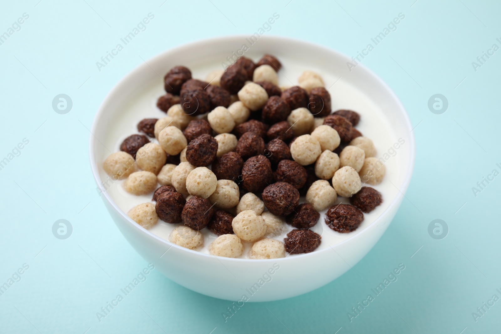 Photo of Breakfast cereal. Tasty corn balls with milk in bowl on light blue background, closeup