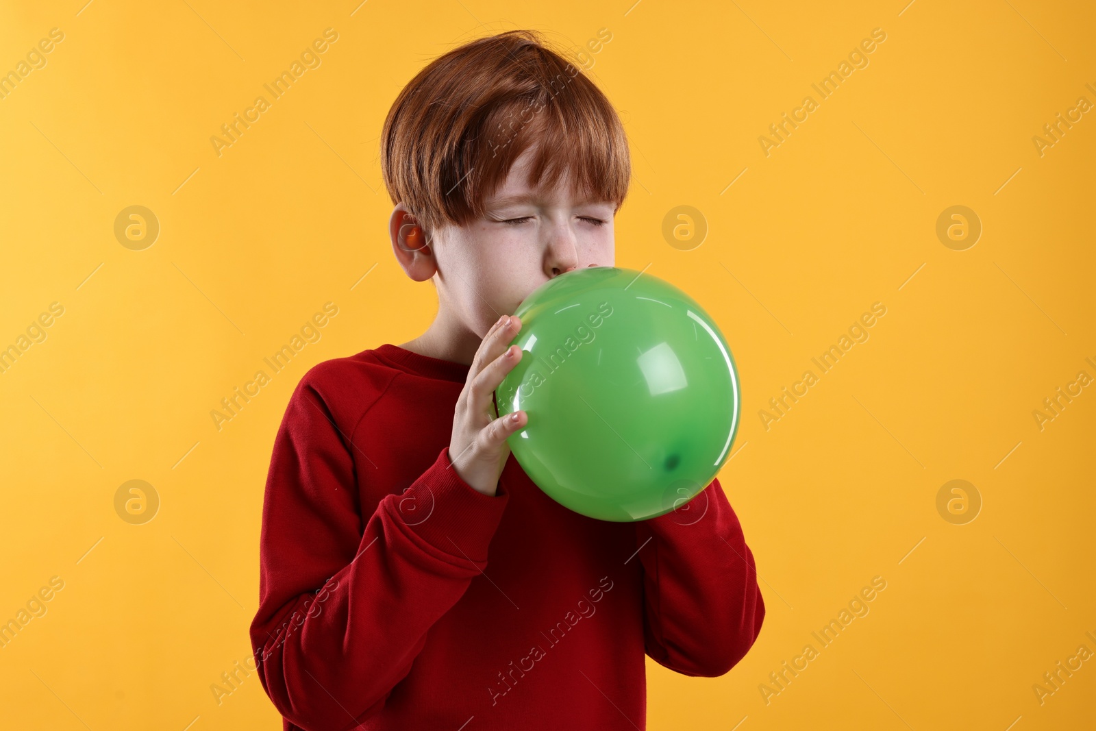 Photo of Boy inflating green balloon on orange background