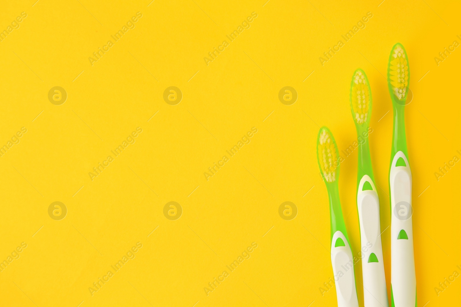 Photo of Toothbrushes on yellow background, flat lay. Space for text