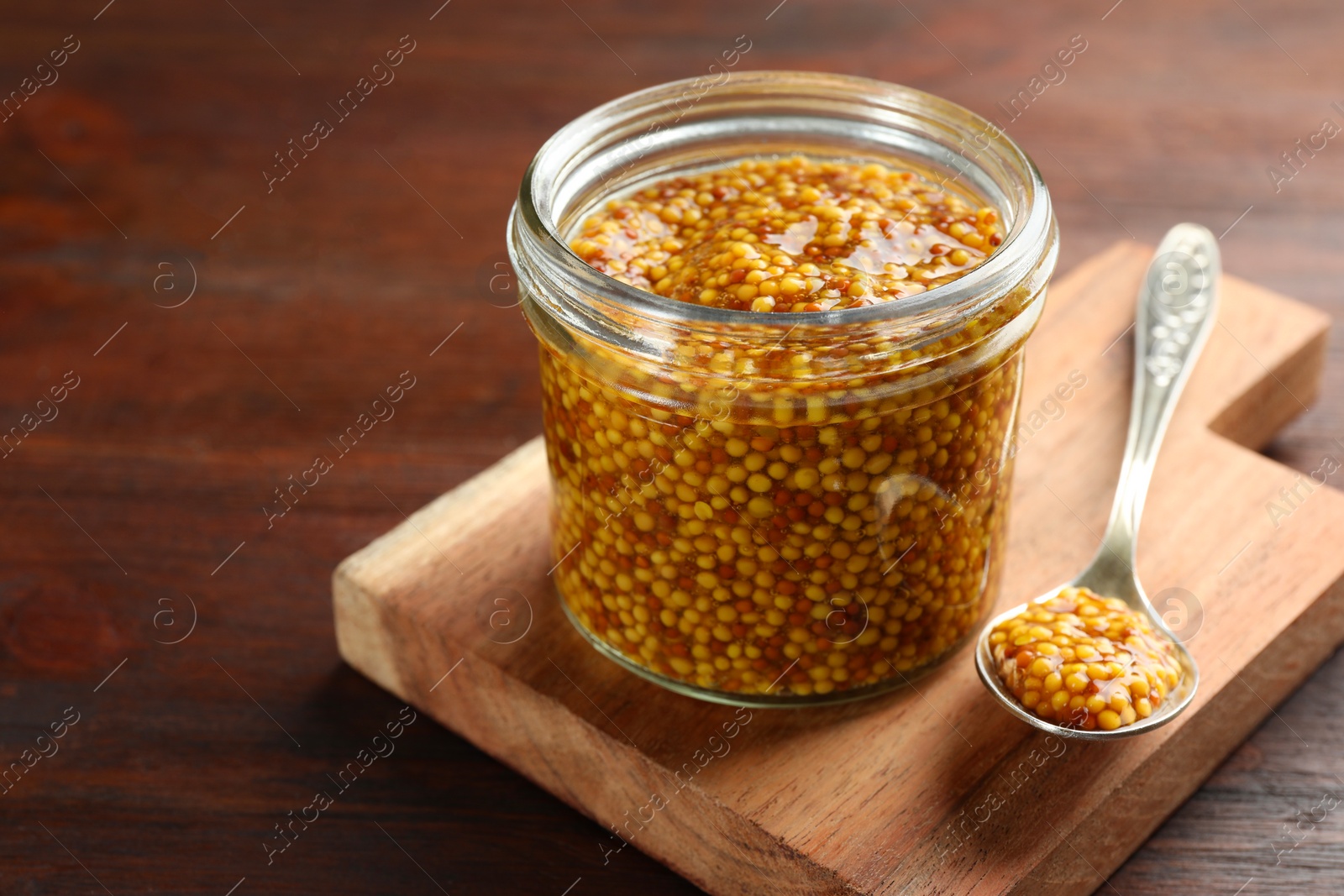 Photo of Jar and spoon with whole grain mustard on wooden table. Space for text