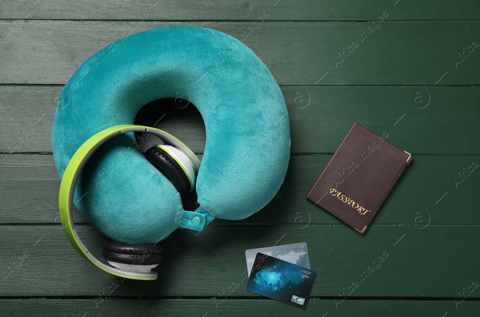 Photo of Turquoise travel pillow, passport and credit cards on green wooden background, flat lay