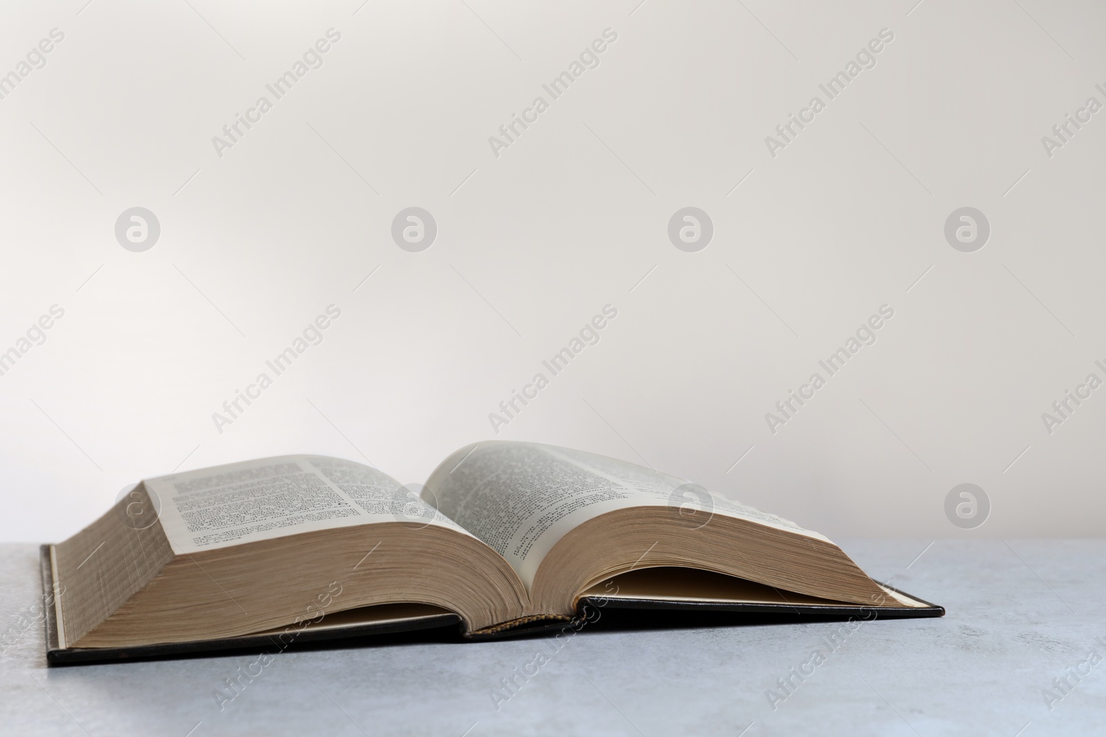 Photo of Open hardcover Bible on light grey table, space for text. Religious book