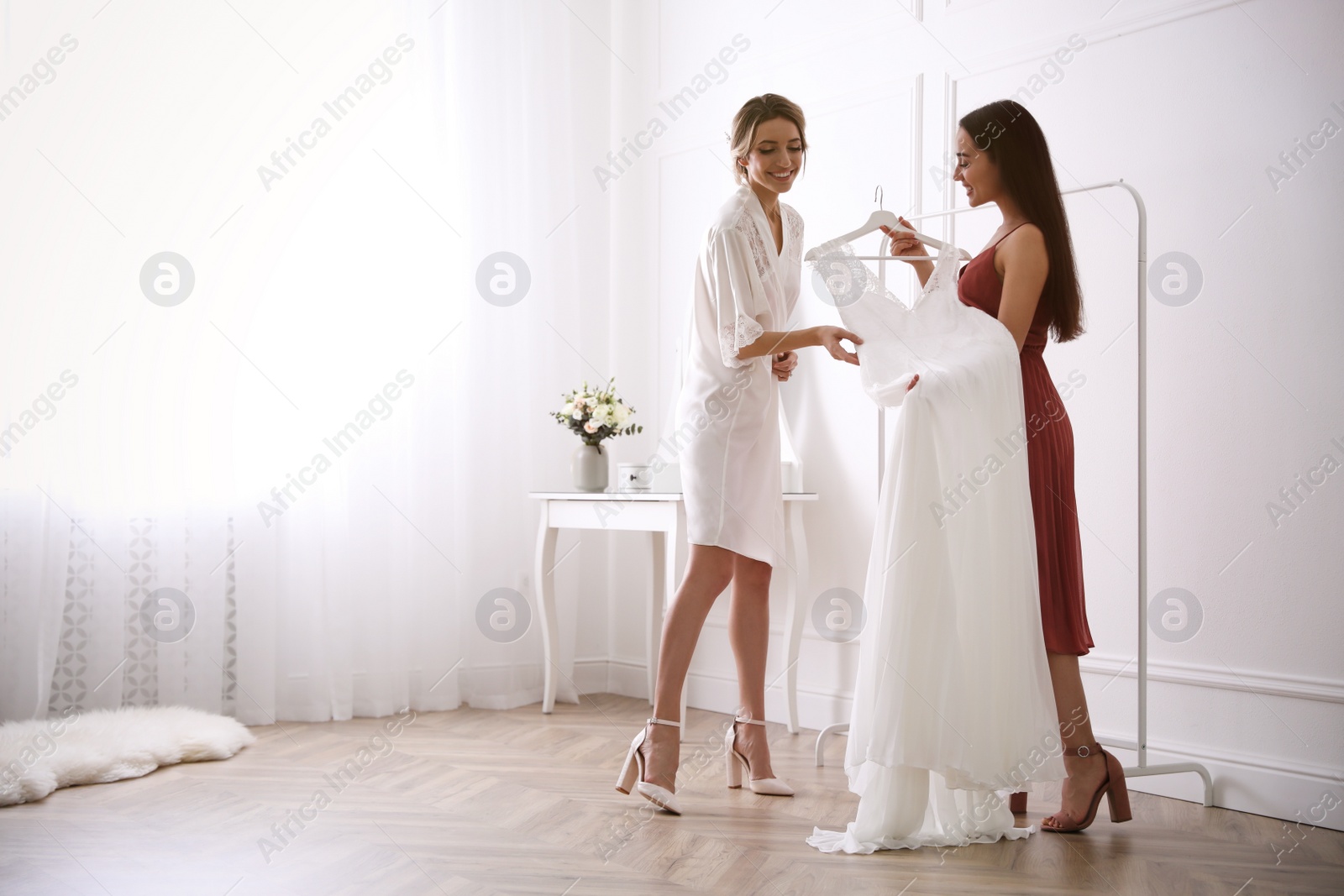 Photo of Young bride and her friend with wedding dress indoors