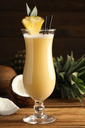 Photo of Tasty Pina Colada cocktail and ingredients on wooden table