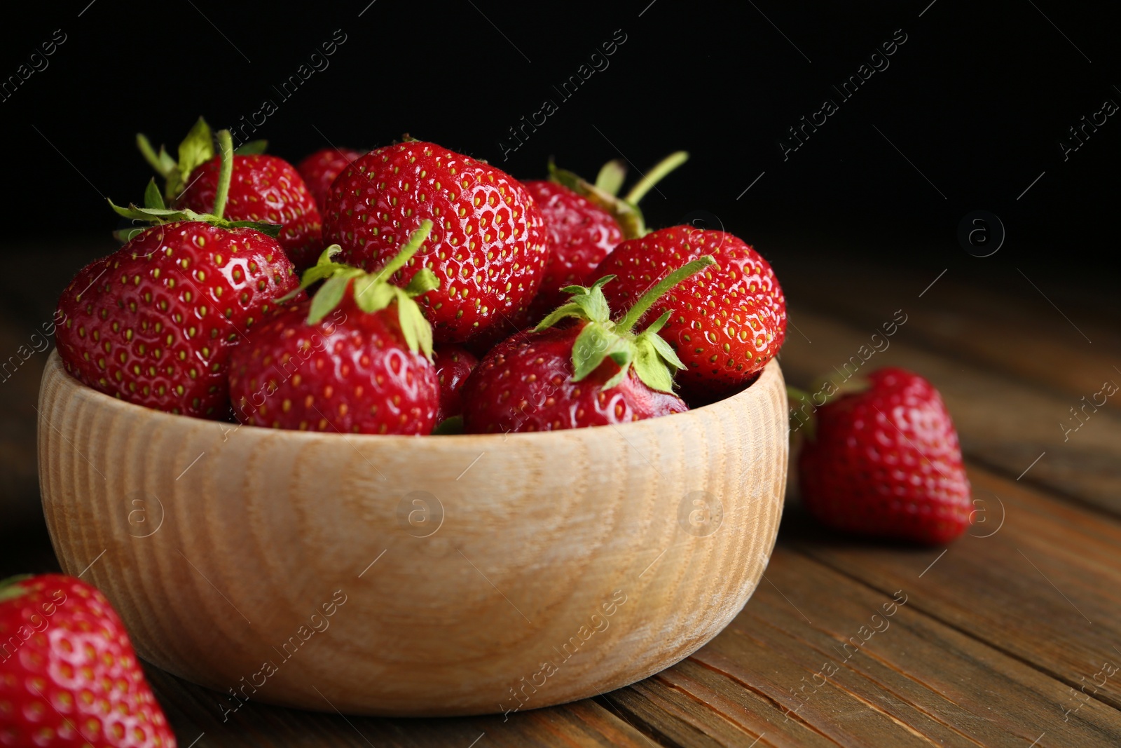 Photo of Delicious ripe strawberries in bowl on wooden table, closeup