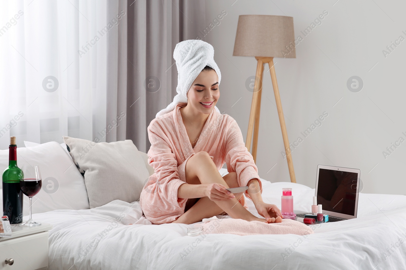 Photo of Beautiful young woman giving herself pedicure on bed at home