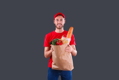 Photo of Delivery man holding paper bag with food products on dark background