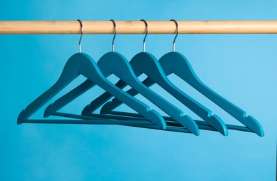 Photo of Bright clothes hangers on wooden rail against light blue background