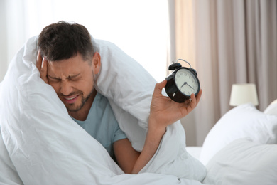 Photo of Sleepy man with alarm clock at home in morning