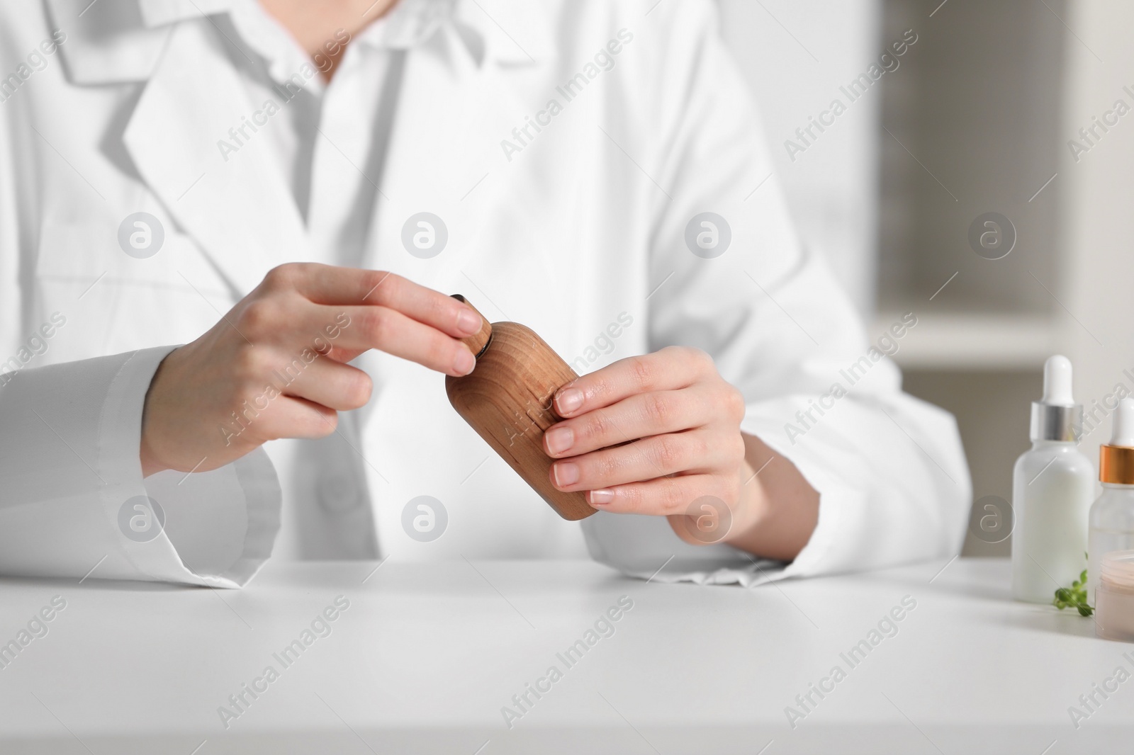 Photo of Dermatologist with bottle of cosmetic product at white table indoors, selective focus. Development and testing
