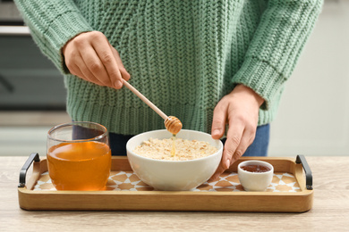 Photo of Woman adding honey to oatmeal at wooden table indoors, closeup